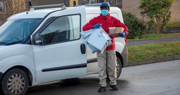 Hampshire, England, UK. 2020, Male courier delivering parcels and packages during Covid-19 epidemic wearing gloves and a mask. - Photo, Image