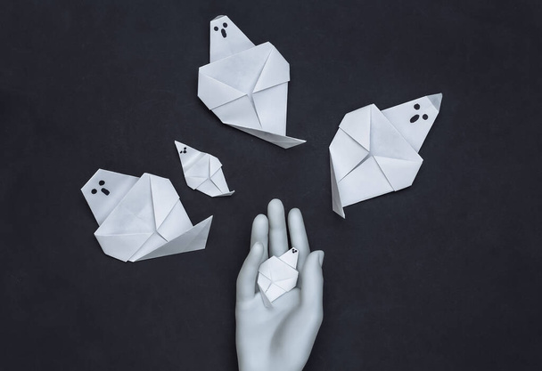 main origami fantômes et main mannequin sur fond noir. Thème Halloween. Vue du dessus - Photo, image