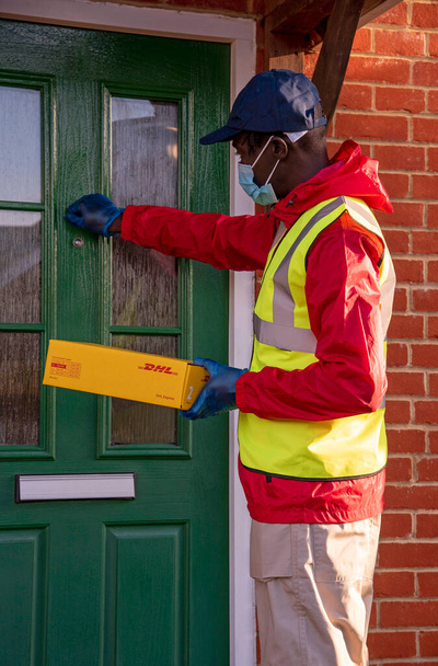 Hampshire, Inghilterra, Regno Unito. 2020, corriere maschio consegna pacchi e pacchi durante l'epidemia di Covid-19 indossando guanti e maschera. - Foto, immagini