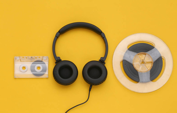 Cuffie stereo e bobina audio magnetica, audiocassetta su sfondo giallo. Vista dall'alto. Posa piatta - Foto, immagini