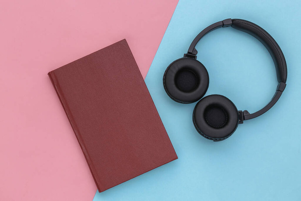Audio libro. Auriculares y un libro sobre fondo pastel azul-rosa. Vista superior. - Foto, Imagen