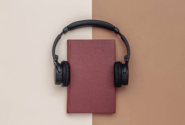 Аудиокнига Наушники и книга на коричневом бежевом фоне. Вид сверху. - Фото, изображение