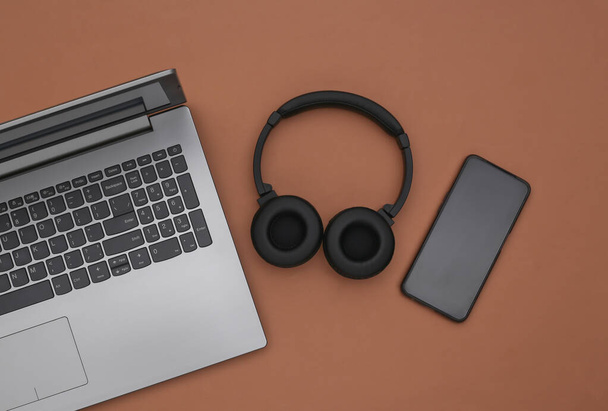 Laptop, smartphone και ασύρματα στερεοφωνικά ακουστικά σε καφέ φόντο. Στο πάνω μέρος. Επίπεδη - Φωτογραφία, εικόνα