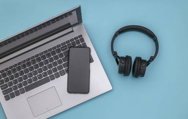 Laptop, smartphone and wireless stereo headphones on a blue background. Top view. Flat lay - Фото, изображение
