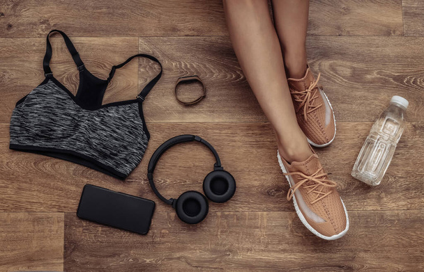 Flat lay composition of woman legs, sports equipment and clothes on a wooden floor. Fitness, sport and healthy lifestyle concept. Top view - Photo, Image
