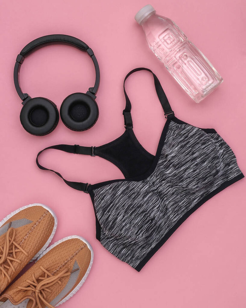 Sujetador deportivo superior, mancuernas, botella de agua y auriculares estéreo sobre fondo rosa. Deporte y fitness. Vista superior. Puesta plana - Foto, Imagen
