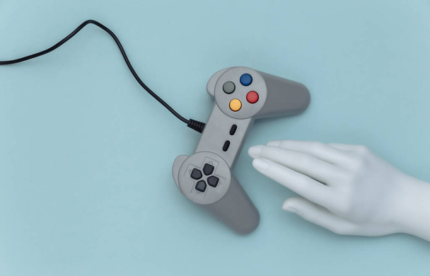 Figurína ruka dotýká retro gamepad na modrém pozadí. Horní pohled. Kreativní umění, minimalismus - Fotografie, Obrázek