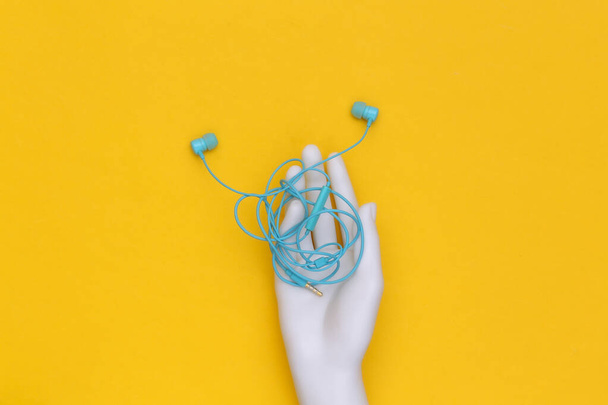 Fones de ouvido emaranhados com fio na mão de manequim branco no fundo amarelo - Foto, Imagem