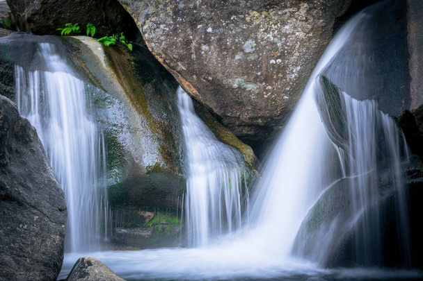 A waterfall with long exposure surrounded by rocks in a forest - Photo, image