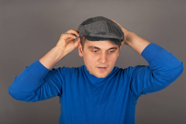 Portrait of a young handsome caucasian man holding his cap in front of grey backgroun - Foto, Bild