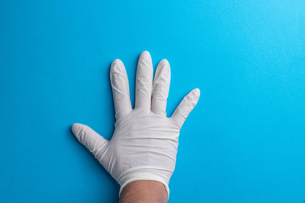 Um tiro de close-up da mão de um médico com luvas de borracha contra um fundo azul - Foto, Imagem
