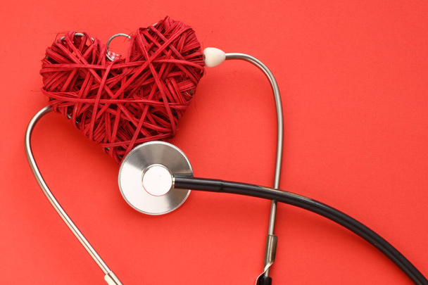 Červené srdce na červeném pozadí, stetoskop na červeném pozadí. Koncepce v medicíně a zdravotnictví. - Fotografie, Obrázek