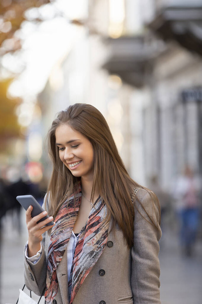 Piękna młoda kobieta korzystająca ze smartfona na ulicy, uśmiechnięta - Zdjęcie, obraz