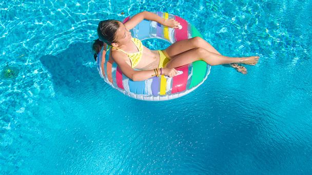 Active girl in swimming pool aerial top view from above, kid swims on inflatable ring donut , child has fun in blue water on family vacation resort - Foto, immagini