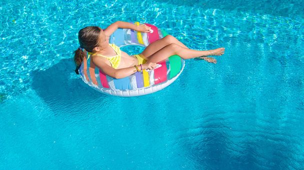 Active girl in swimming pool aerial top view from above, kid swims on inflatable ring donut , child has fun in blue water on family vacation resort - 写真・画像