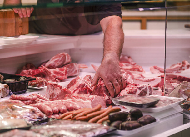 A closeup of a hand of a shop assistant choosing meat from the shop window - Photo, image