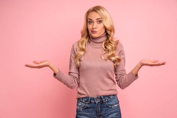 Portrait of a confused young casual girl shrugging shoulders isolated over pink background. - Photo, Image