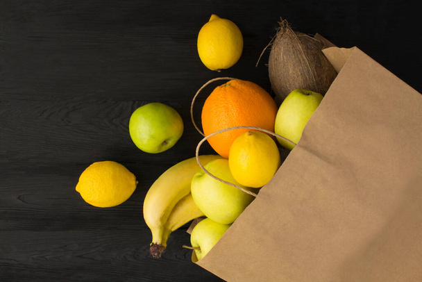 Бумажный пакет с фруктами на черной деревянной поверхности - Фото, изображение