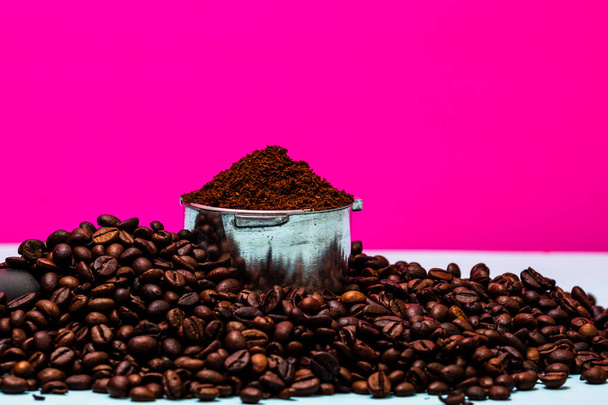 Koffiebonen en portafilter met gemalen koffie in een compositie op een roze achtergrond. - Foto, afbeelding