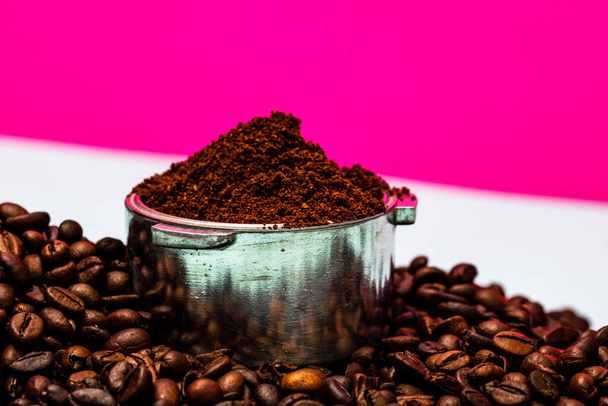 Coffee beans and portafilter with ground coffee in a composition on a pink background. - Photo, Image