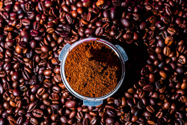 Hintergrund mit gemahlenem Kaffee im Portafilter umgeben von gerösteten Kaffeebohnen, - Foto, Bild