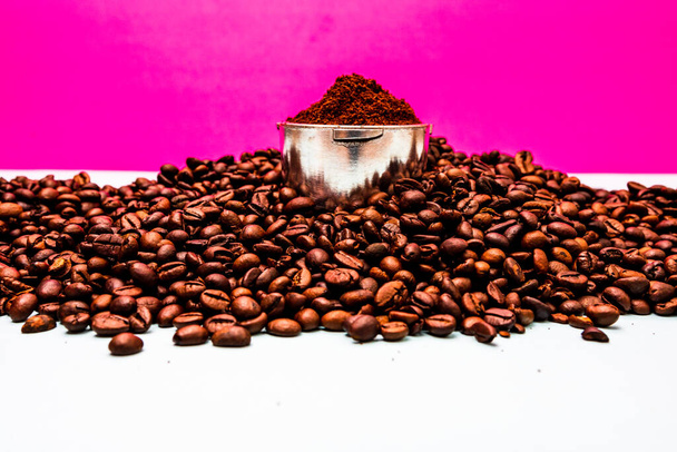 Кофейные зерна и портативный фильтр с молотым кофе в композиции на розовом фоне. - Фото, изображение