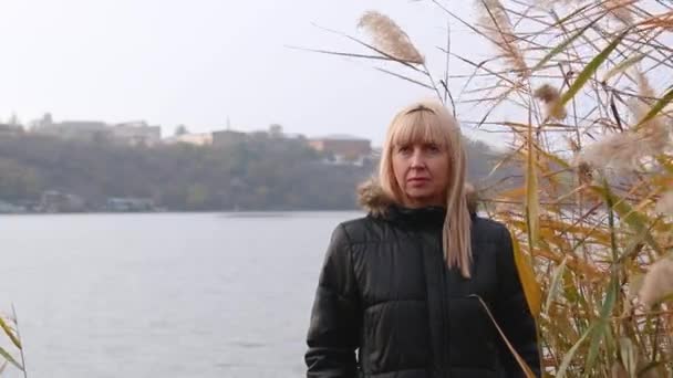 Kobieta stoi na brzegu rzeki w trzciny i myśli. nastrój jesienny i depresja - Materiał filmowy, wideo