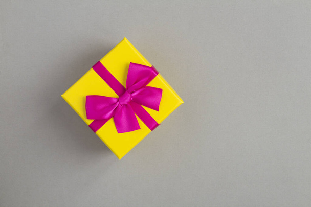 Primer plano en caja de regalo amarilla con cinta rosa sobre fondo gris - Foto, imagen