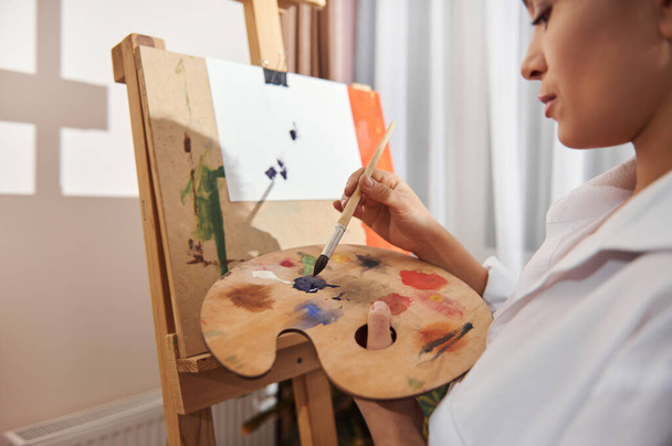 Focus op penseel. Brunette vrouw schilderen thuis. - Foto, afbeelding