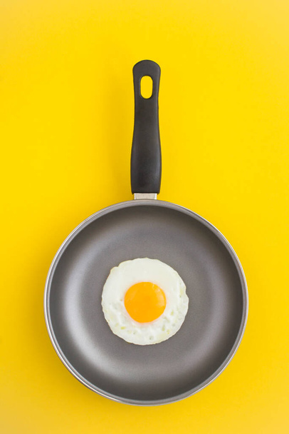 Вид зверху сковороди зі смаженим яйцем на жовтому фоні
 - Фото, зображення