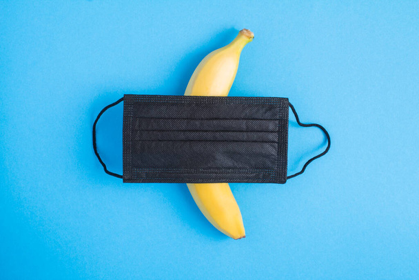 Μαύρη ιατρική μάσκα και μπανάνα στο κέντρο του μπλε φόντου - Φωτογραφία, εικόνα