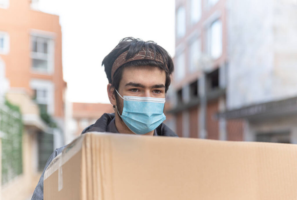 Üniformalı ve maskeli teslimatçı büyük bir teslimat kutusu taşıyor. - Fotoğraf, Görsel