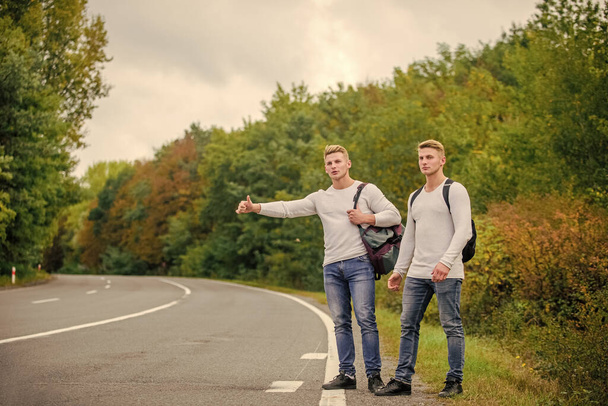 type of adventure. On the road. Enjoying summer hike. Looking for transport. twins walking along road. stop car with thumb up gesture. hitchhiking and stopping car with thumbs up gesture - Zdjęcie, obraz
