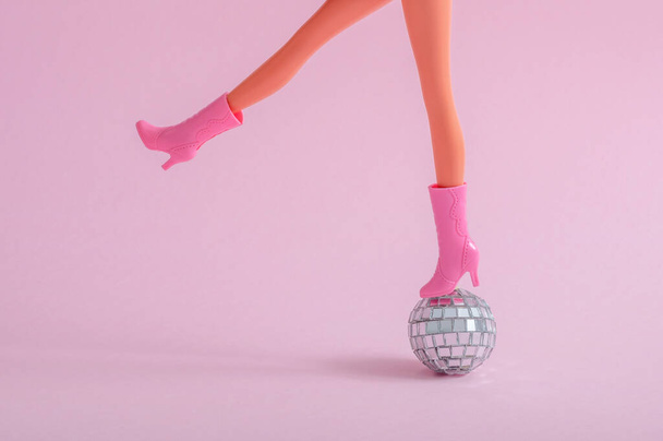 Plastic doll feet on a small disco ball on a pink background - Foto, Imagem