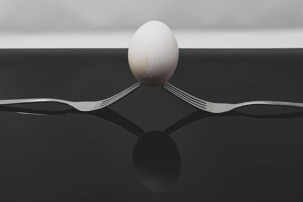 A closeup of an egg balancedon two forks with a grey background - concept: balance - Foto, imagen