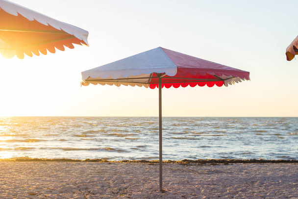 Барвиста пляжна парасолька на піщаному порожньому пляжі на сході сонця
 - Фото, зображення