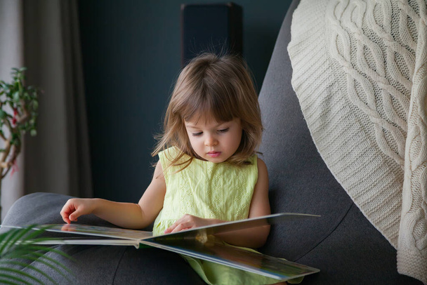 Little cute baby girl in yellow dress reading a book at home - Φωτογραφία, εικόνα
