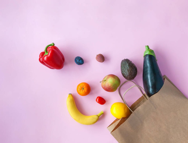 Shopping paper bag with different fruits and vegetables falling out of it. Pink background, flat lay. - Foto, afbeelding