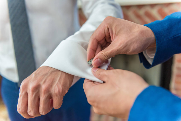 A closeup shot of best man helping groom in button cufflinks - wedding day concept - Valokuva, kuva