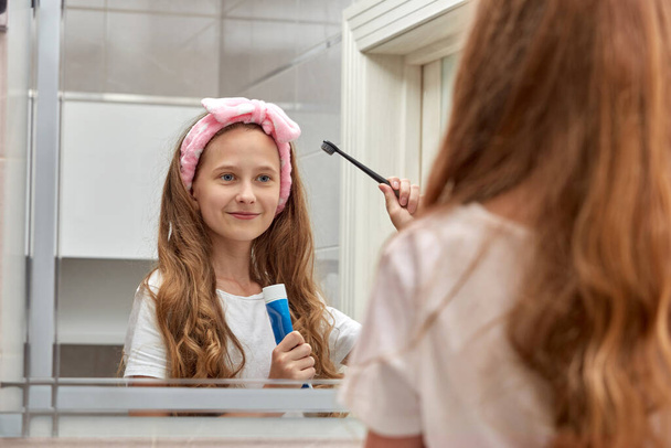 Blonde teen in the bathroom brushing her teeth. Care of the oral cavity. - Foto, Bild