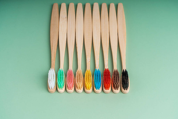 A set of Eco-friendly antibacterial toothbrushes made of bamboo wood on a light green background. Environmental care trends. - Φωτογραφία, εικόνα