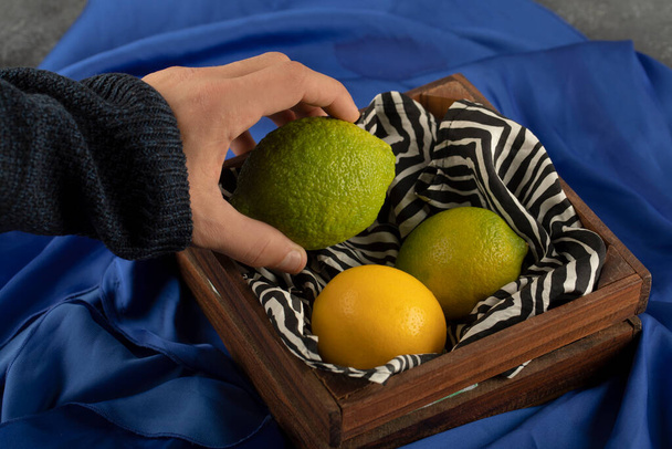 Man hand taking a lime from a wooden basket - Foto, imagen