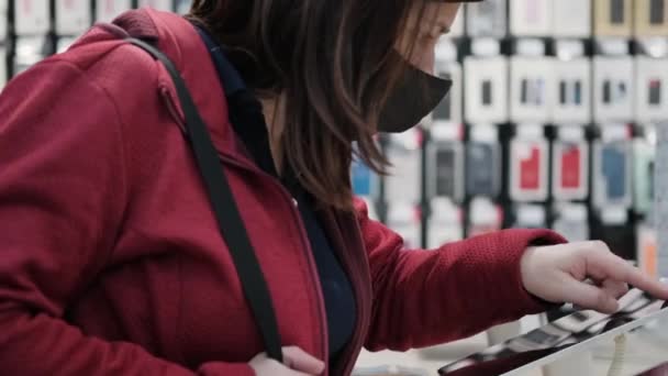 Maszkos nő vesz egy tabletet egy modern elektronikai boltban. - Felvétel, videó