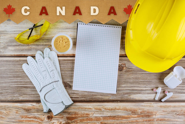 Ofis masasında boş defterle çalışan mühendis Kanada 'da koruyucu sarı kaskla mutlu İşçi Bayramı tatildir. - Fotoğraf, Görsel