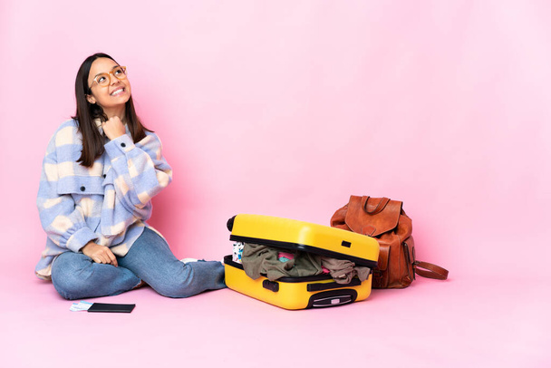 Viaggiatore donna con una valigia seduta sul pavimento guardando in alto sorridendo - Foto, immagini