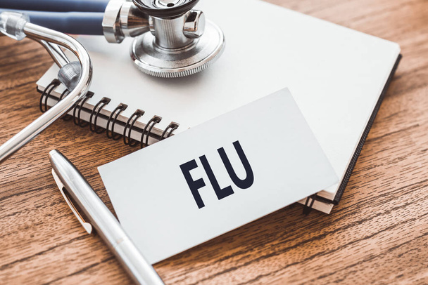 FLU is written in a notebook on a wooden table next to a pen and a stethoscope. Medical concept. - Fotó, kép