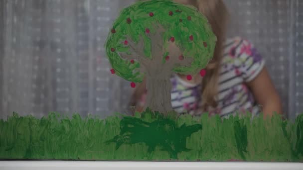 Παιδική ηλικία, δημιουργικότητα, τη φύση, την άνοιξη, το καλοκαίρι έννοια - γκρο πλαν χαριτωμένο κοριτσάκι 3-4 ετών επιστήσει με ακρυλικά χρώματα στο τζάμι του παραθύρου. προσχολική παιδική ζωγραφική τοπίο: ήλιος, δέντρο, σύννεφο, βροχή, λουλούδι - Πλάνα, βίντεο