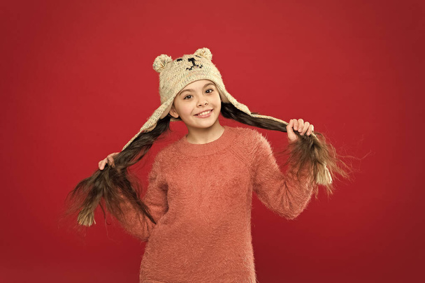 Happiness and joy. Winter outfit. Small child long hair wear hat red background. Cute model enjoy winter style. Adorable small bear. Little kid wear knitted hat. Little girl winter fashion accessory - Fotoğraf, Görsel