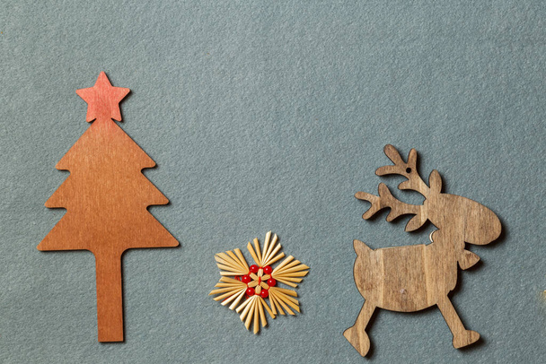 Ξύλινα ειδώλια για τη διακόσμηση του χριστουγεννιάτικου δέντρου. Χριστουγεννιάτικο δέντρο, ελάφι και αστέρι από άχυρο. Διάταξη σε γκρι φόντο με χώρο. - Φωτογραφία, εικόνα