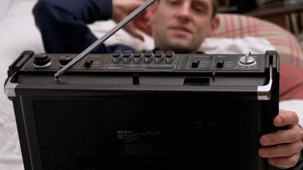 Hombre cansado acostado en la cama presiona el botón Play en la vieja radio cassette con antena - Metraje, vídeo